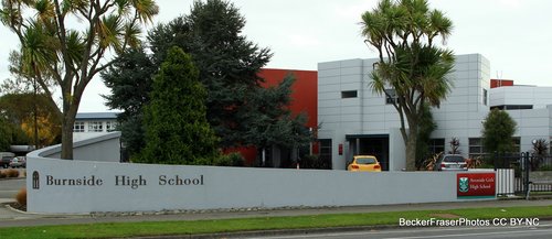 Burnside High School&#x27;s front gate. Tied to the wall further down is a temporary red and green sign reading "Avonside Girls High School." It has Avonside Girls&#x27; logo on it.